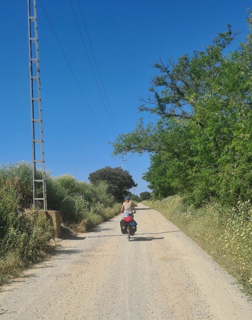 Fietser met kampeerspullen op de fiets fietst over een gravelweg in Spanje.