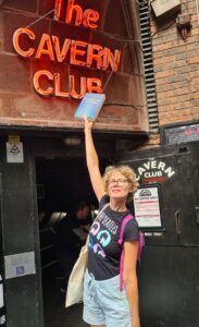 Auteru Laura Alblas houdt haar roman Het magsiche verhaal van de Verteller omhoog voor de ingang van The Cavern Club in Liverpool.